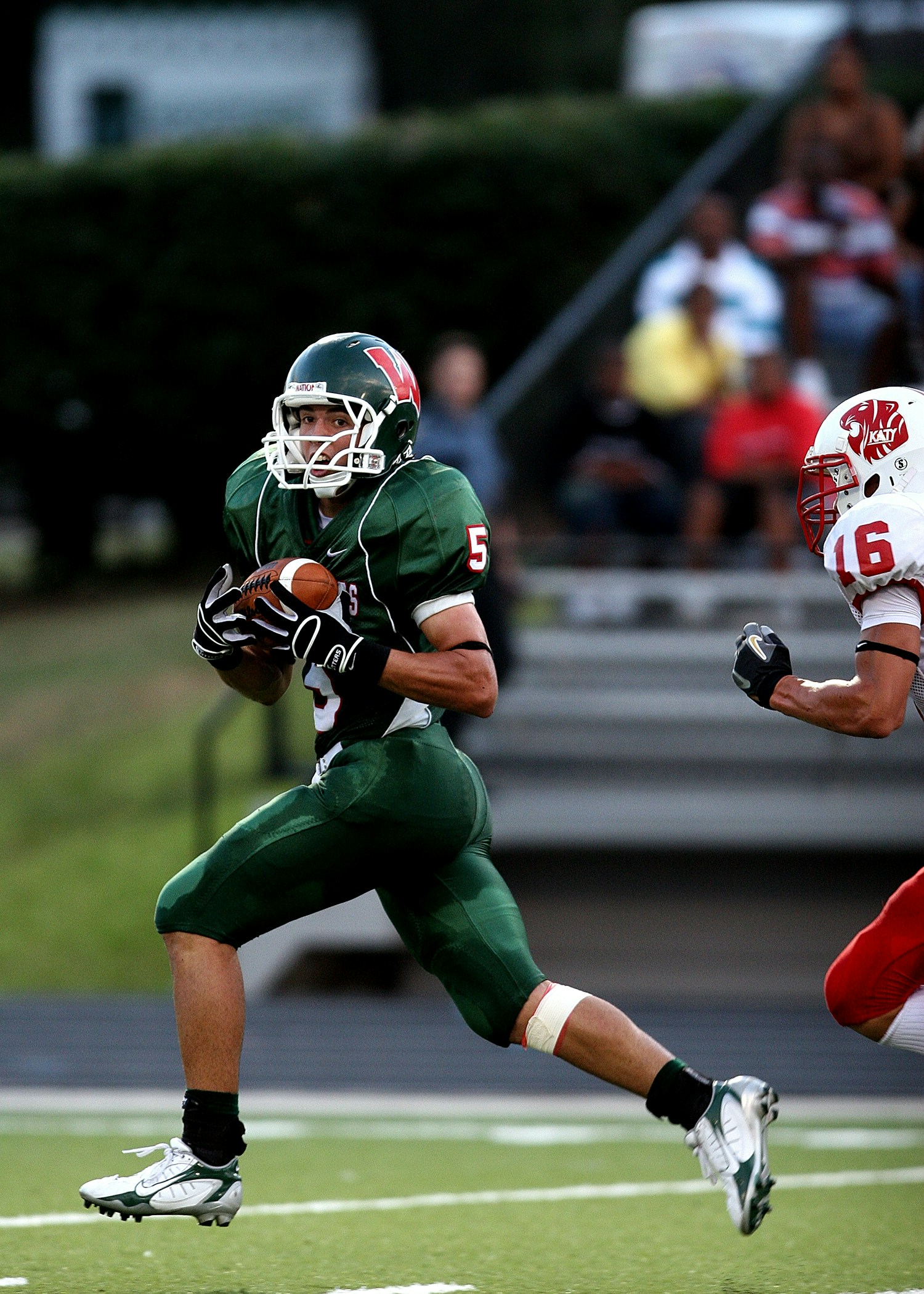 Two football players, one having dark hair and the other having brown hues, wearing green and black jerseys, white and gre...